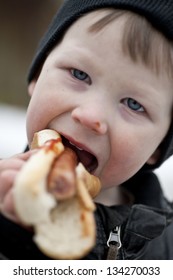 Young Boy Eating A Hotdog With Ketchup Outdoors