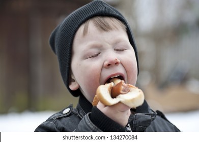 Young Boy Eating A Hotdog With Ketchup Outdoors