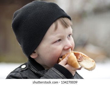 Young Boy Eating A Hotdog Outdoors Looking Aside