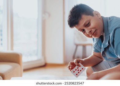 A young boy engaged in a card game at home, enjoying a moment of leisure and fun. Bright natural light fills the cozy room. - Powered by Shutterstock