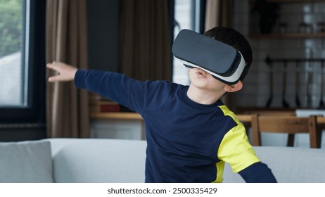 A young boy engaged in a virtual reality experience at home. He wears VR goggles and has his arms outstretched, appearing to navigate or interact with the virtual world. - Powered by Shutterstock