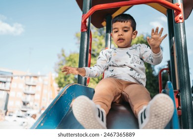 Young boy enjoys a sunny day at the playground, sliding down a colorful slide - Powered by Shutterstock