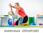 Young boy exercising with female physical therapist during therapy session. Child occupational physical therapy. Bilateral coordination.