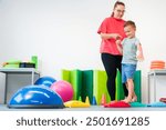 Young boy exercising with female physical therapist during therapy session. Child occupational physical therapy. Bilateral coordination.