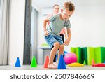 Young boy exercising with female physical therapist during therapy session. Child occupational physical therapy. Bilateral coordination.