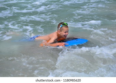 Young Boy Experiences Boogie Boarding For The First Time At Madeira Beach, Florida.  He Has A Smile Plastered All Over His Face.  Blue Board And Blue Snorkle Glasses.