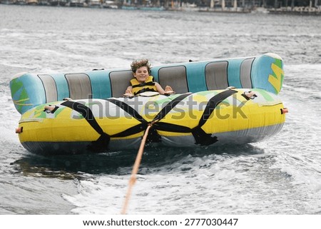 Young boy exudes joy while riding an inflatable tube towed by a boat in the ocean. Happy school child having fun in adventure water park on the sea