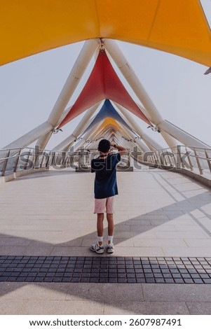 A young boy is facing away from the camera and taking a photo of the arches of the Atal Bridge - the new pedestrian bridge on the Sabarmati River