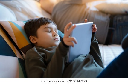 Young boy falling sleep while watching cartoon on tablet, Tried kid lying in bed play game online, Child sleeping while reading e-book on digital tablet, School boy relaxing at home