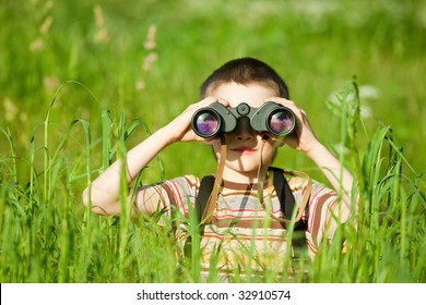 Young boy in a field looking through binoculars
