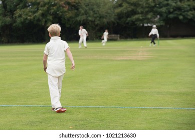 young boy fielding in game of cricket with batsman and bowler in the background - Powered by Shutterstock