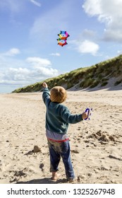 Young Boy Flying A Colourful Kite On The Beach At Bamburgh, Northumberland, UK