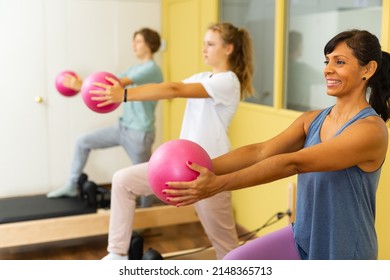 Young boy and girl doing exercises on pilates reformers and using small fitness balls. They're standing in row with their trainer and repeating her moves.