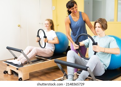Young boy and girl doing exercises on pilates reformers and using special rings and fitness balls. Their trainer hispanic woman correcting them.