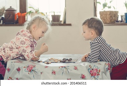 Young Boy And Girl Playing Checkers Or Draughts Both Leaning Over The Table Looking At The Board As They Plan Their Next Move