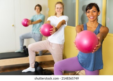Young boy and girl standing in row with pilates trainer latin woman and using small fitness balls for exercising.