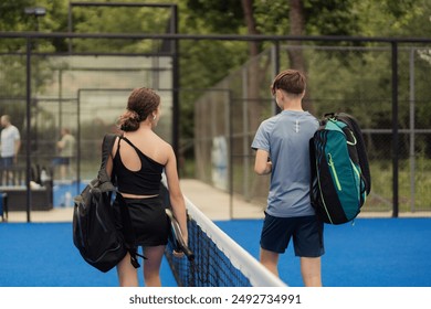 Young boy and girl walking on a padel tennis court carrying sports bags. Active lifestyle and outdoor sports concept. - Powered by Shutterstock