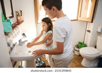 Young boy and girl washing hands together at bathroom sink, highlighting the importance of hygiene and cleanliness in daily routines. - Powered by Shutterstock