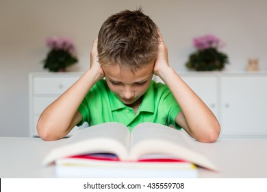 Young Boy In Green Polo Shirt Having Serious Learning Difficulties While Trying To Read A Textbook From School.