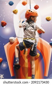 Young Boy Hanging On Rope At Indoor Climbing Wall. Kid In Helmet Having Fun At Bouldering Wall. Child Learning At Climbing Class. Family Sport, Healthy Lifestyle, Happy Family. 