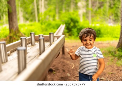 Young boy having fun interacting with a wooden sensory play table with metal cylinders in a natural forest environment, promoting learning and exploration