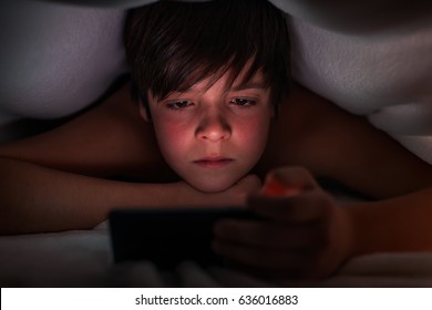 Young Boy Hiding Under The Blanket Using His Phone At Night Time - Closeup