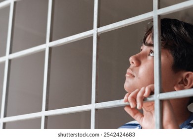 A young boy in his early teens was clinging to the bars of a locked iron door and looking up to the sky outside, punishment from his parents, detention of teens and freedom of child concept. - Powered by Shutterstock