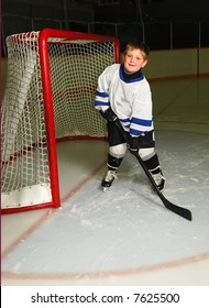 A Young Boy In Hockey Pose In Front Of The Net Of A Dark Arena