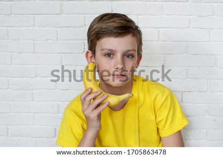 Young boy holding banana on his ears. Funny boy holding banana as horns. Yellow style. Food concept. Boy in yellow t-shirt. Funny expressions. Healthy food