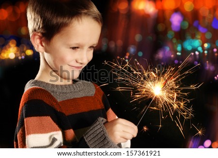 Young boy holding burning sparkler on festive lights background