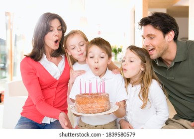 Young boy holding a cake and blowing out the candles as he is celebrating his birthday with his family. - Powered by Shutterstock
