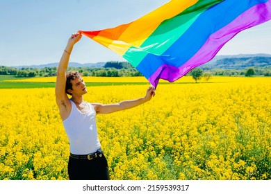 Young Boy Holding The LGBT Gay Rainbow Flag On Yellow Rapeseed Field In Spring. Happiness, Freedom And Love Concept For Same Sex Couples. Lifestyle Outdoors.