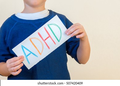 Young Boy Holds ADHD Text Written On Sheet Of Paper. ADHD Is Attention Deficit Hyperactivity Disorder. 