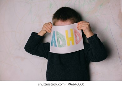 Young Boy Holds ADHD Text Written On Sheet Of Paper. ADHD Is Attention Deficit Hyperactivity Disorder.