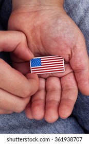 Young Boy Holds American Flag Badge (USA Flag Pin) In His Hands. Close Up.