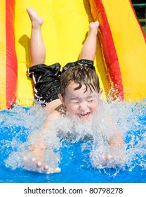 Young Boy Or Kid Has Fun Splashing Into Pool After Going Down Water Slide During Summer