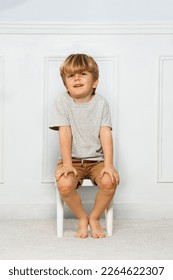 Young boy with knee having patch covering a scratch, while his hands and fingers lay on knees smiling sitting on a stool