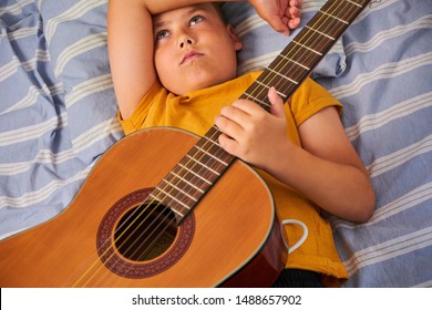 Young Boy Laying Down And Holding A Guitar In A Bed 