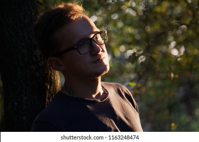 young boy leaned back against a tree at sunset in the forest