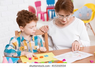 Young Boy Learning New Words Playing With Colorful Letters. Older Teacher Sitting Next To Him