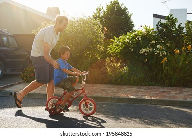 young boy learning to ride bicycle as father teaches him in the suburb street having fun. - Shutterstock ID 195848825