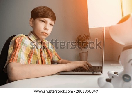 Young boy learning stem education and programming skills, typing on a laptop with a personal robot companion on the desk, focusing on the future of technology and ai