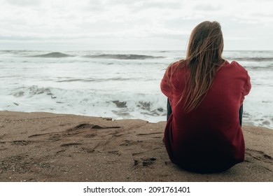 Young boy with long hair sitting on his back looking at the sea