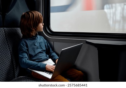 Young Boy Looking Out of Train Window with Laptop.