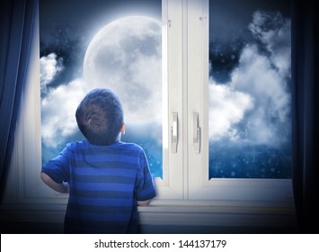 A Young Boy Is Looking Out Of The Window At A Big Moon In The Dark Night With Stars And Space For An Astronomy Or Imagination Concept.