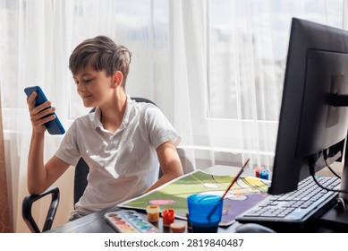 Young boy looking at a smartphone while painting at home. Concept of digital distraction, excessive screen time, reduced attention span, children's creativity, technology use, child development, balancing screen time and creative activities, digital wellbeing and modern parenting.