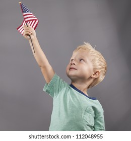 A young boy looks up at an American flag that he holds proudly above his head.
