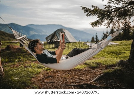 Young boy lying down in a hammock on the mountain and read a book