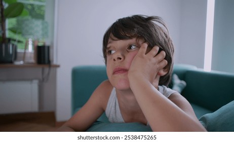 Young boy lying on couch, head propped on hand, eyes gazing upward, reflecting a moment of curiosity and daydreaming in a casual and cozy indoor environment - Powered by Shutterstock