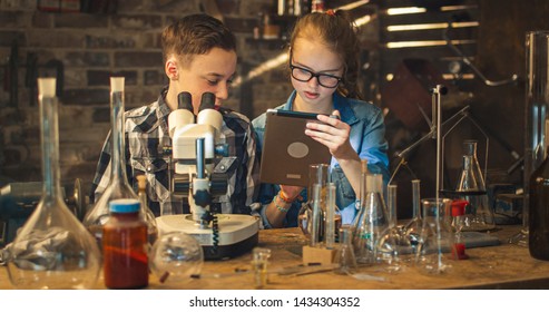 Young Boy Is Making Chemistry Experiments While Girl Is Looking At A Tablet Computer In A Garage At Home.